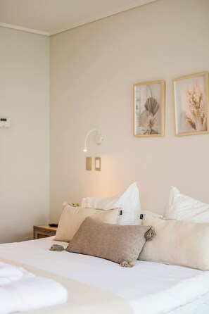 Habitación de hotel con cama, almohadas, una mesita de noche, una lámpara de pared y dos cuadros enmarcados.