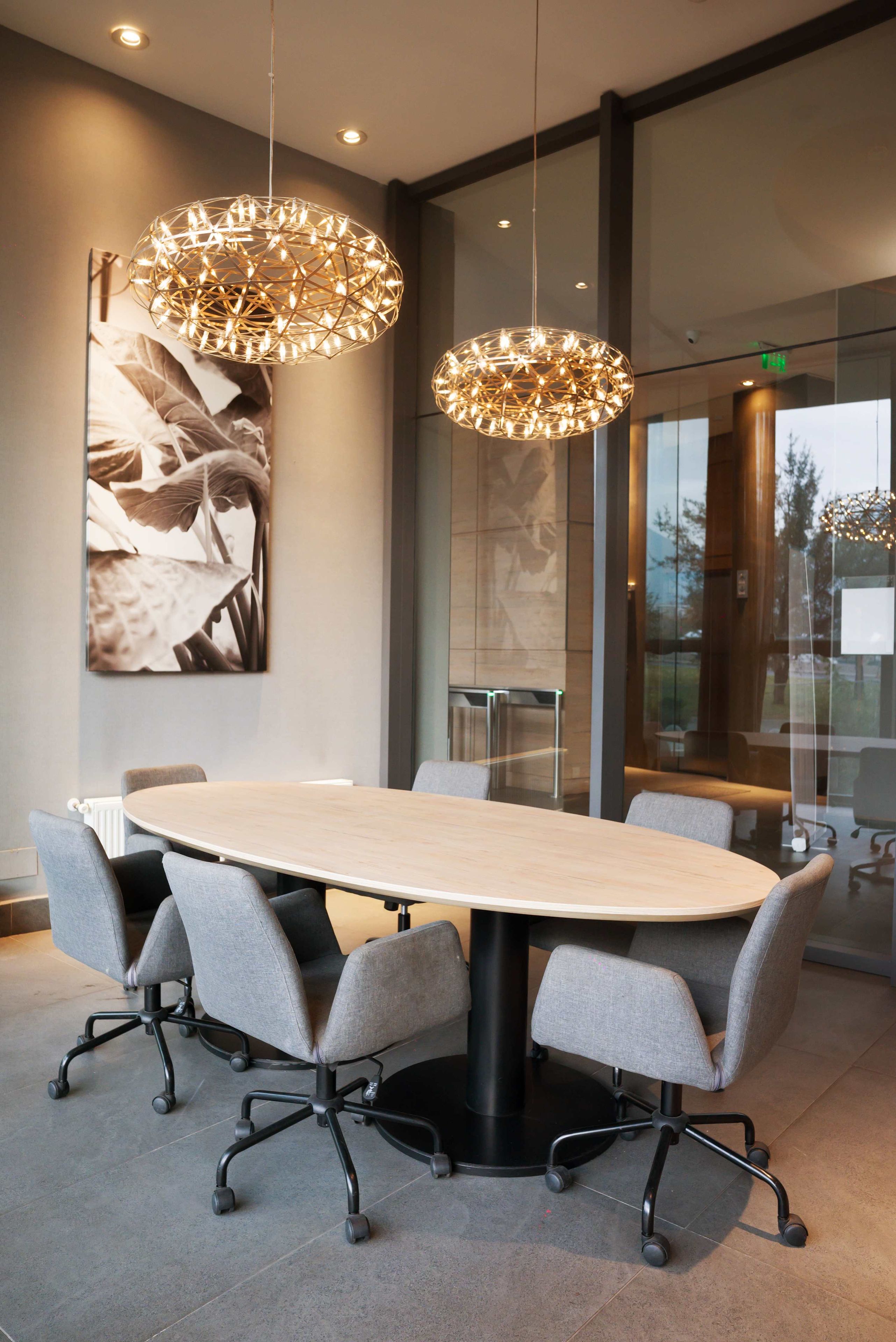 Une salle de conférence dotée d’une grande table ovale, de chaises de bureau grises et de deux lampes suspendues.