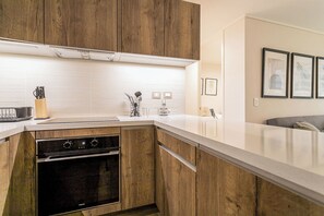 Une cuisine moderne avec des meubles en bois, un four encastré et un plan de travail blanc.
