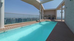 A rooftop infinity pool with a city view, surrounded by glass railings and wooden decking. - Chic Las Condes Apt: 2BR, 2BA, Sleeps 5 (Las Condes)