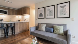 A modern living space with a grey sofa, wooden flooring, a kitchen area with a microwave, and three framed artworks on the wall. - Chic Las Condes Apt: 2BR, 2BA, Sleeps 5 (Las Condes)