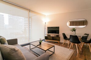 Una sala de estar moderna con sofá, mesa de centro, televisor y comedor con sillas y una mesa.
