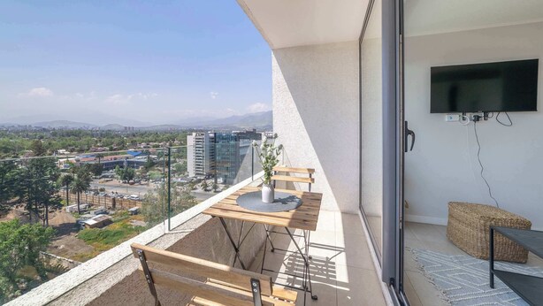Un balcon avec une table en bois, une chaise, un téléviseur et une vue sur le paysage urbain.