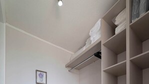 Une pièce avec une armoire blanche, un petit meuble et une étagère où sont pliés des vêtements.