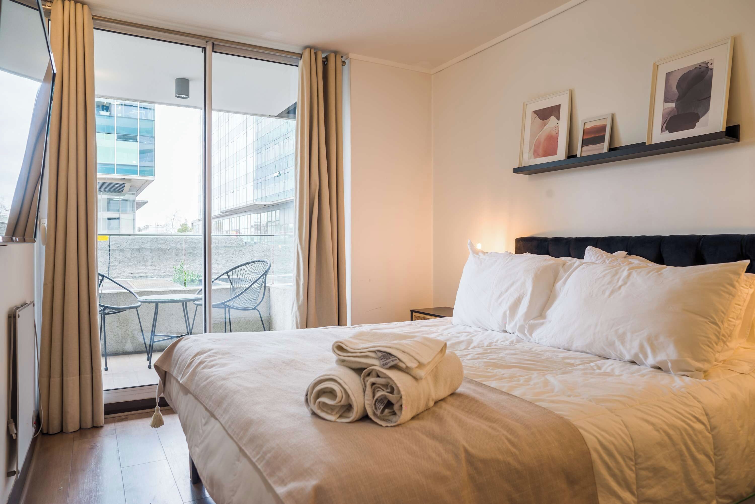 A hotel room with a bed, a small table, a chair, and a view of the outside.