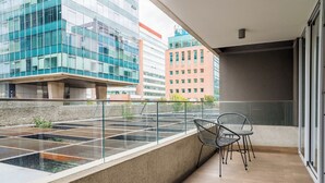 Un balcón con vista a edificios modernos, barandilla metálica y dos sillas.