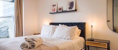 A hotel room with a bed, a nightstand, a lamp, and a wall-mounted shelf with pictures.