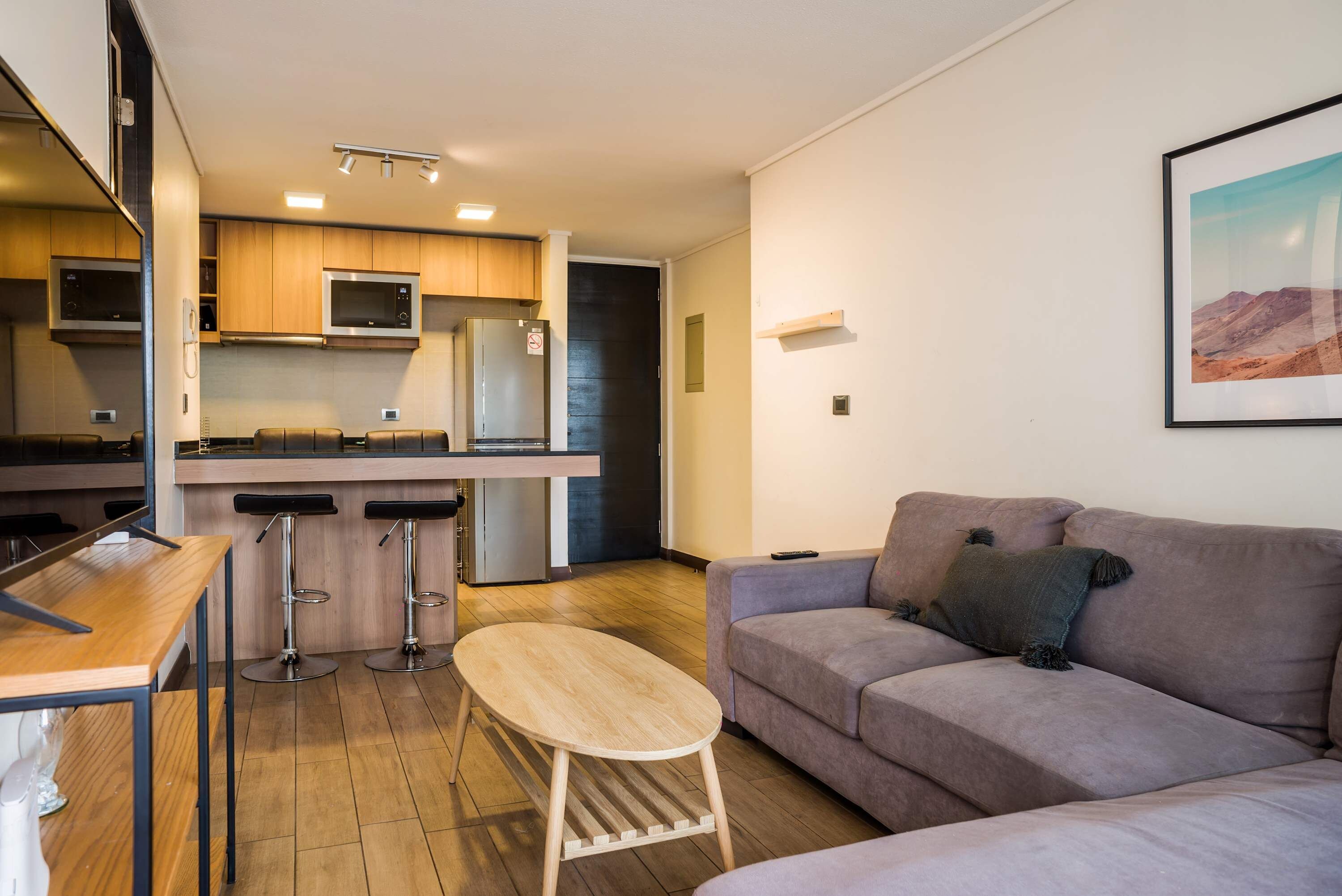 A compact living space with a kitchenette, a dining area with stools, a sofa, and a coffee table.