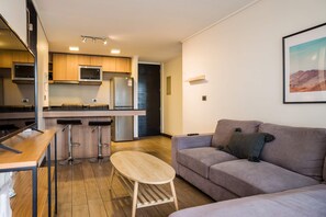 A compact living space with a kitchenette, a dining area with stools, a sofa, and a coffee table.