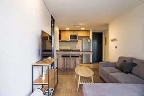Un espace de vie compact comprenant un coin cuisine, un canapé, une petite table et un téléviseur.