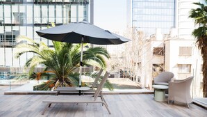 A modern lounge area with a lounge chair, a small table, and a large umbrella. - Chic Urban Retreat 1BR Apartment in Providencia (Providencia)
