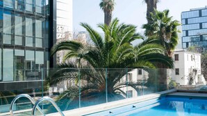 A swimming pool with a glass barrier, surrounded by palm trees and modern buildings. - Chic Urban Retreat 1BR Apartment in Providencia (Providencia)