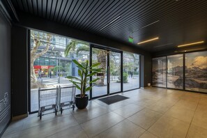 A spacious lobby with large windows, a potted plant, and a view of the street outside.