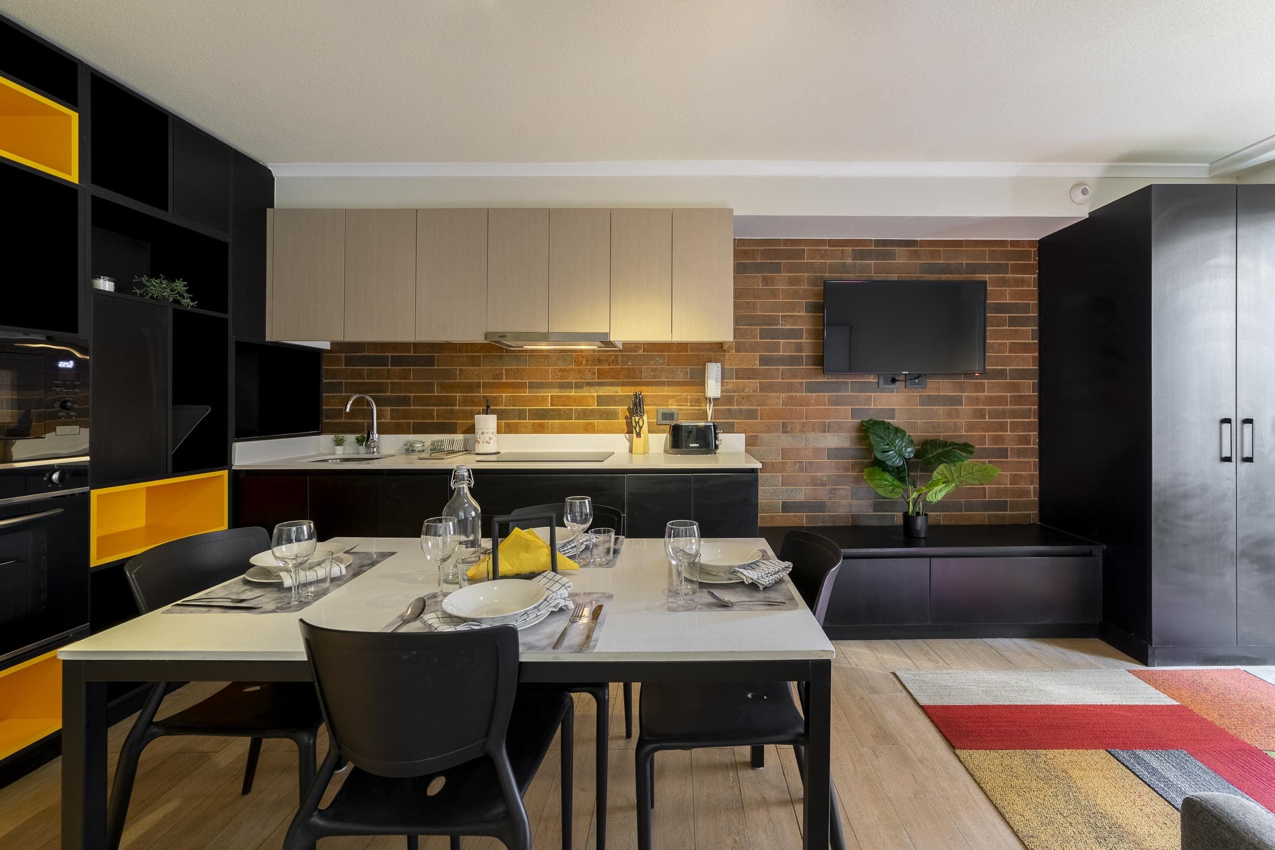 Une cuisine moderne avec un coin repas, un téléviseur à écran plat fixé au mur et un four encastré.
