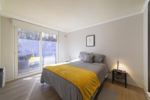 A bedroom with a bed, a bedside table, a lamp, a picture on the wall, and a sliding glass door leading to an outdoor area.