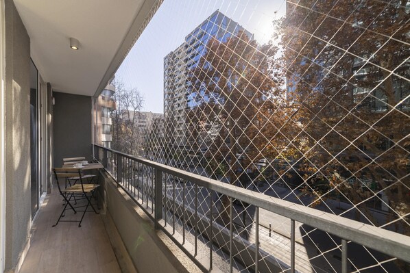 A balcony with a metal railing, a table with chairs, and a view of a building and trees.