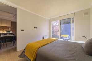 Une chambre à coucher avec un lit, un bureau avec une chaise, une fenêtre donnant sur un beau paysage et un balcon.