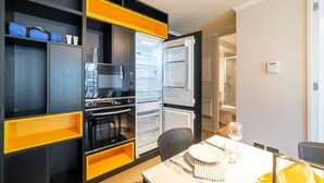 Una cocina moderna con electrodomésticos integrados, un comedor con una mesa dispuesta para dos personas y un baño a la vista.