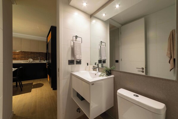 Un baño moderno con lavamanos, espejo y retrete blancos.