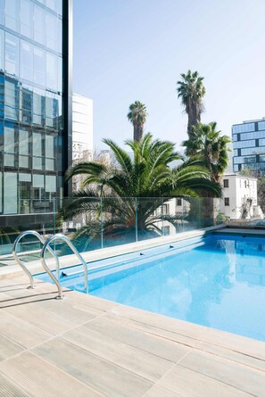 Ein Swimmingpool mit Glasbarriere, umgeben von Palmen und modernen Gebäuden.
