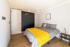 A bedroom with a bed, a nightstand, a wardrobe, and a framed picture on the wall. - Modern Apartment in Central Providencia with Pool (Providencia)