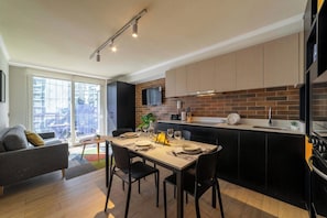 A modern kitchen with a dining area, a sofa, and a view of the outside.