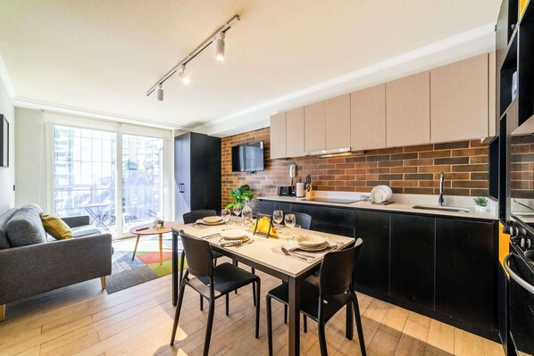 A modern kitchen with a dining area, a sofa, and a large window.