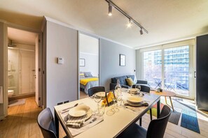 A modern interior with a dining area, a living space with a sofa and a bed, and a large window offering a view of the outside.