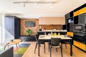 A modern kitchen with a brick wall, a flat-screen TV, and a dining area with a table set for four. - Modern Apartment in Central Providencia with Pool (Providencia)