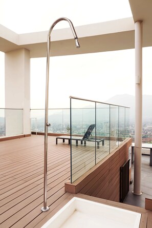Een dakterras met een glazen balustrade, een bank en een metalen buitenkraan.