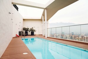 Une piscine sur le toit offrant une vue sur la ville, avec une terrasse en bois et des plantes en pot.