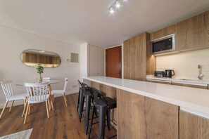 A modern kitchen with a white countertop, wooden cabinets, a microwave, and a coffee maker. - Comfortable Apartment in Las Condes: Pool and Gym! (Las Condes)