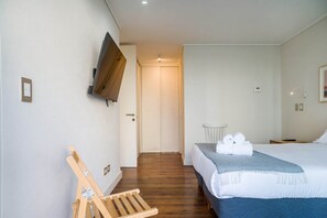 A hotel room with a bed, a TV mounted on the wall, a wooden chair, and a door leading to another room. - Comfortable Apartment in Las Condes: Pool and Gym! (Las Condes)