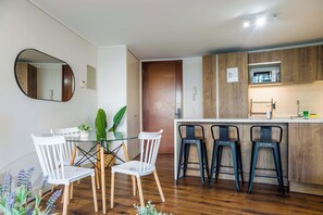 A modern kitchen with a central island, bar stools, and a dining area with chairs. - Comfortable Apartment in Las Condes: Pool and Gym! (Las Condes)
