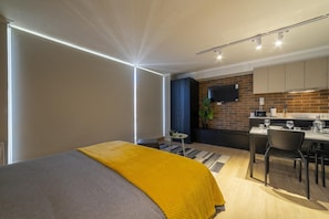 A modern bedroom with a bed, a bedside table, and a window with blinds. - Charming Studio Retreat in Providencia's Heart (Providencia)