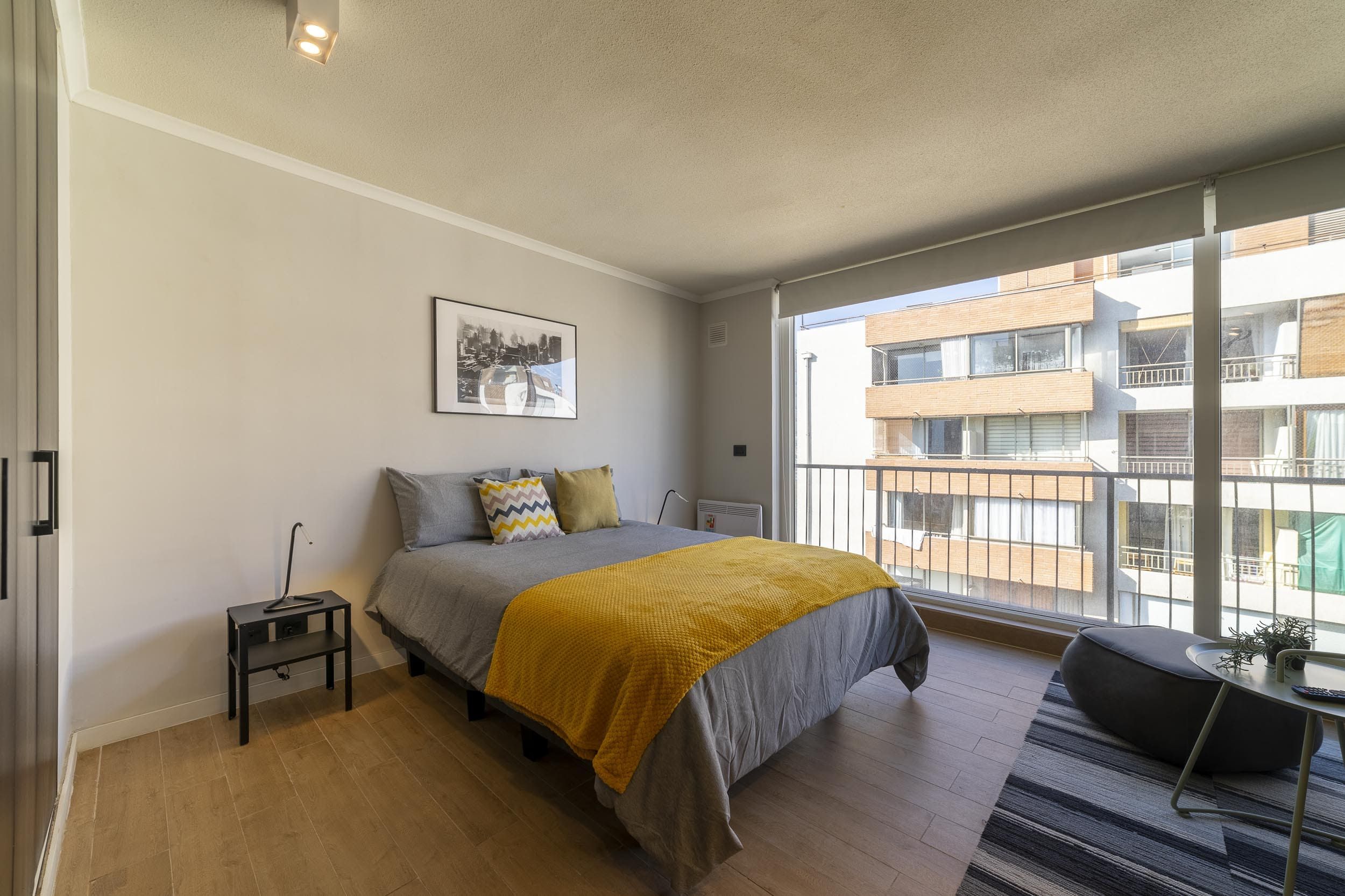 Une chambre à coucher avec un lit, une table de chevet et une fenêtre donnant sur un immeuble d’habitation.