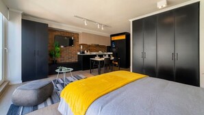 A modern bedroom with a large bed, a small seating area, and a kitchenette in the background. - Charming Studio Retreat in Providencia's Heart (Providencia)