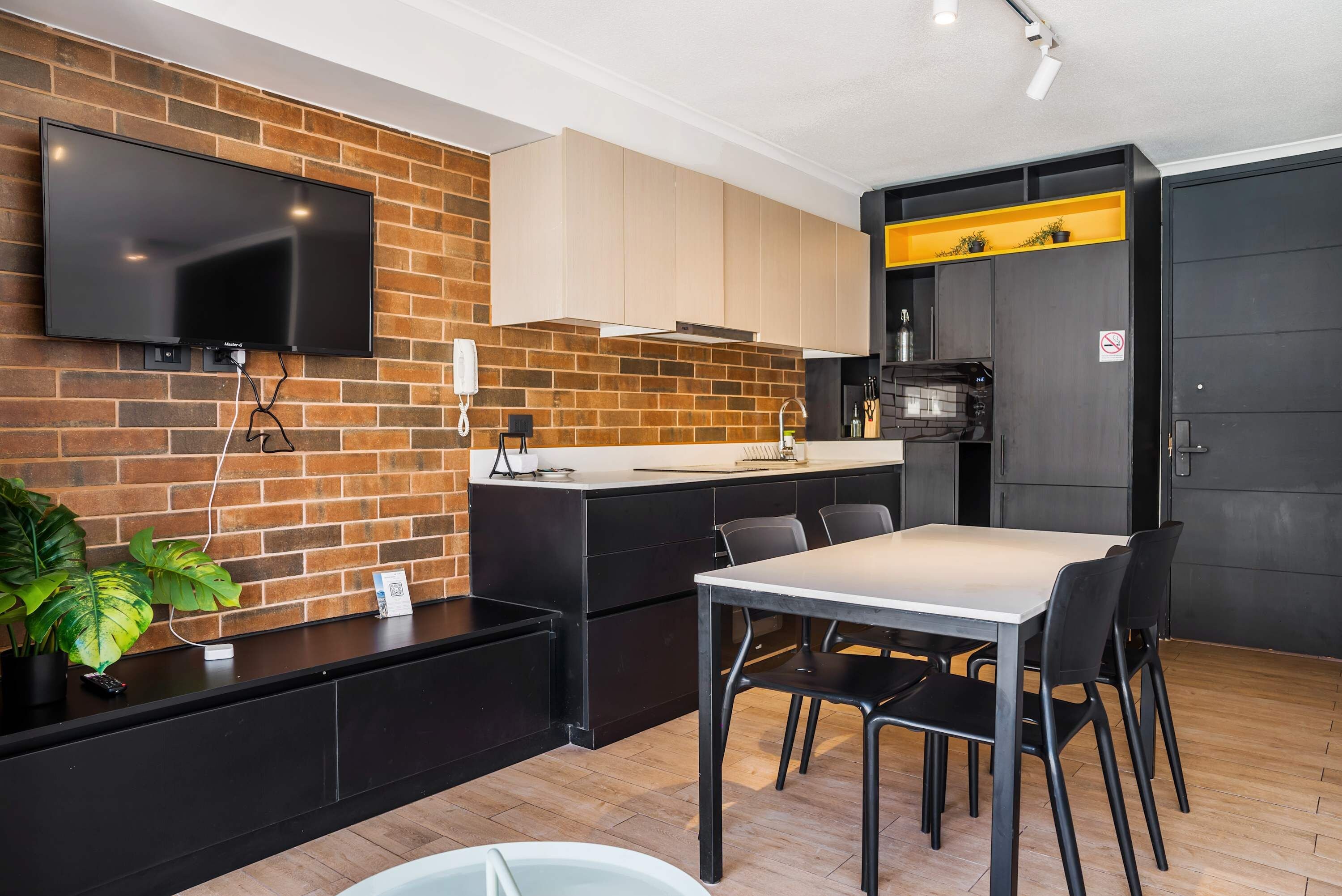 A modern kitchen with a brick wall, a flat-screen TV, and a dining area with a table and chairs.