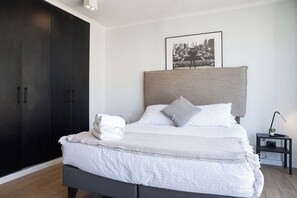 A modern bedroom with a large bed, a dark wardrobe, and a framed picture on the wall.