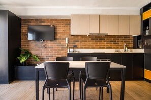 A modern kitchen with a brick wall, a flat-screen TV, and a dining area with a table and chairs. - Stylish and Cozy Studio Apartment in Providencia (Providencia)