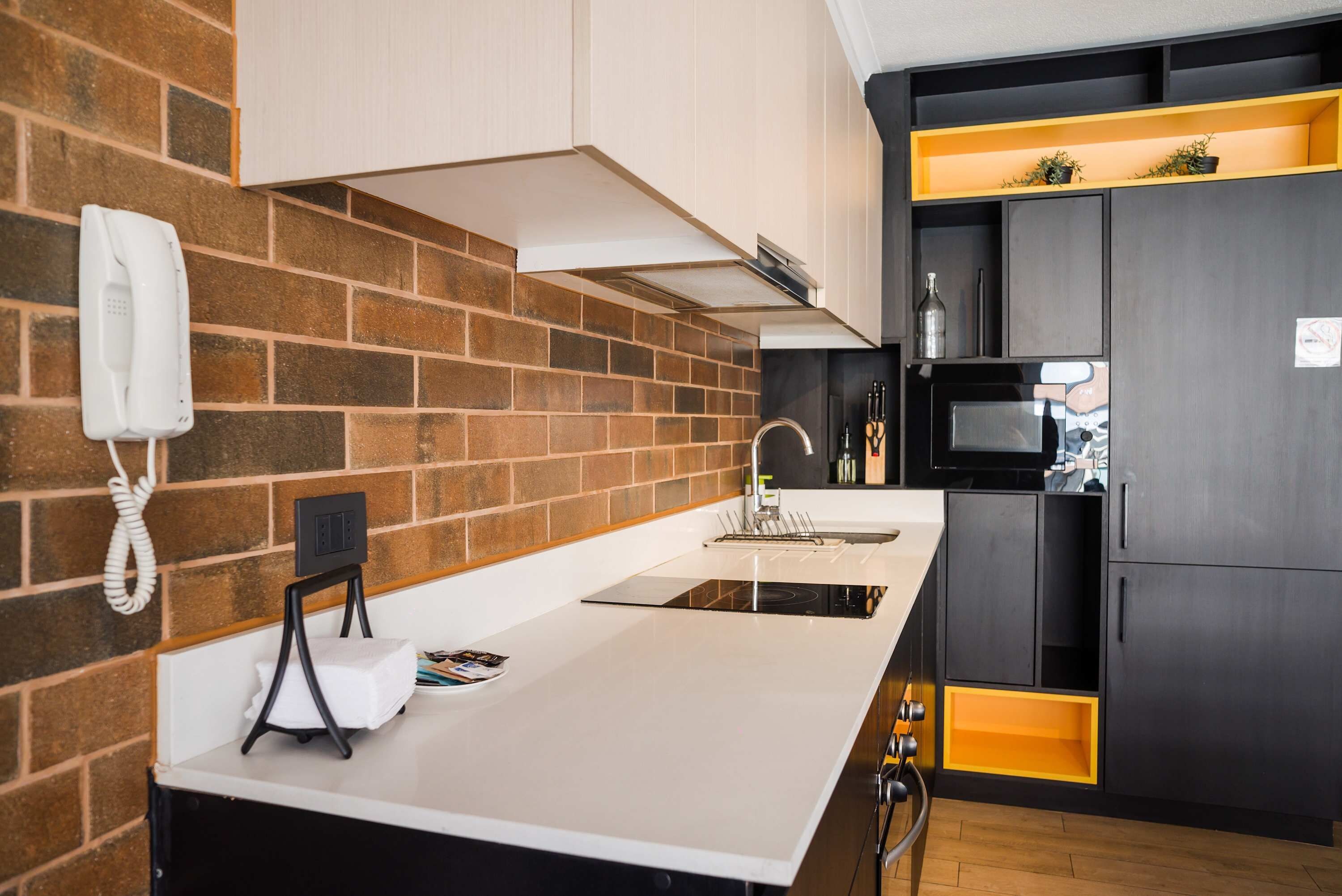 Una cocina moderna con salpicadero de ladrillo, encimera blanca y refrigerador negro.