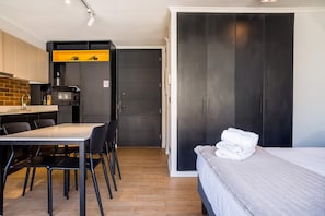 A compact room with a bed, a dining table with chairs, a kitchenette, and a wardrobe.