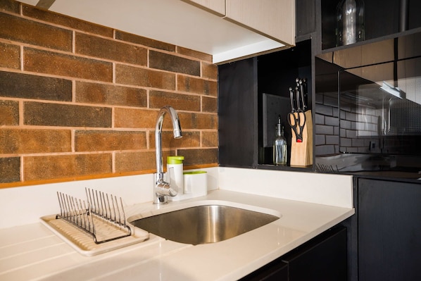 A kitchen with a stainless steel sink, a knife block, and a brick backsplash.