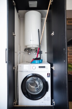 A compact, enclosed laundry room with a front-loading washing machine and a stacked dryer.