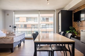 A modern apartment with a balcony, a dining area, a kitchen with a TV, and a bed with towels. - Stylish and Cozy Studio Apartment in Providencia (Providencia)