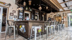 Un espace bar doté d’un comptoir en bois, de tabourets en métal et de luminaires suspendus.