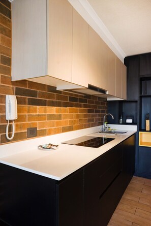 Une cuisine moderne avec un mur de fond en briques, une cuisinière encastrée et un plan de travail blanc.