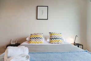 A neatly made bed with two pillows, a bedside table with a lamp, and a framed picture on the wall.