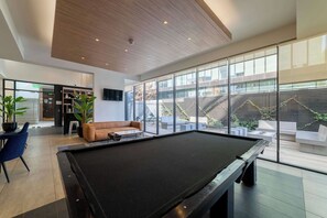 Un espace piscine intérieur moderne, doté d’une table de billard, de sièges et offrant une vue sur l’extérieur.
