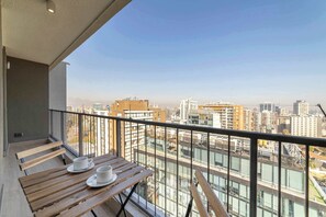Ein Balkon mit Tisch und Stühlen mit Blick auf eine Stadtlandschaft aus Gebäuden und einem klaren Himmel.